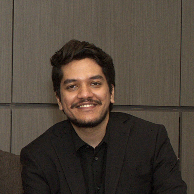Two women sitting together in a cozy, well-lit workspace, smiling and collaborating over a laptop, with a coffee cup and a bowl on the table.