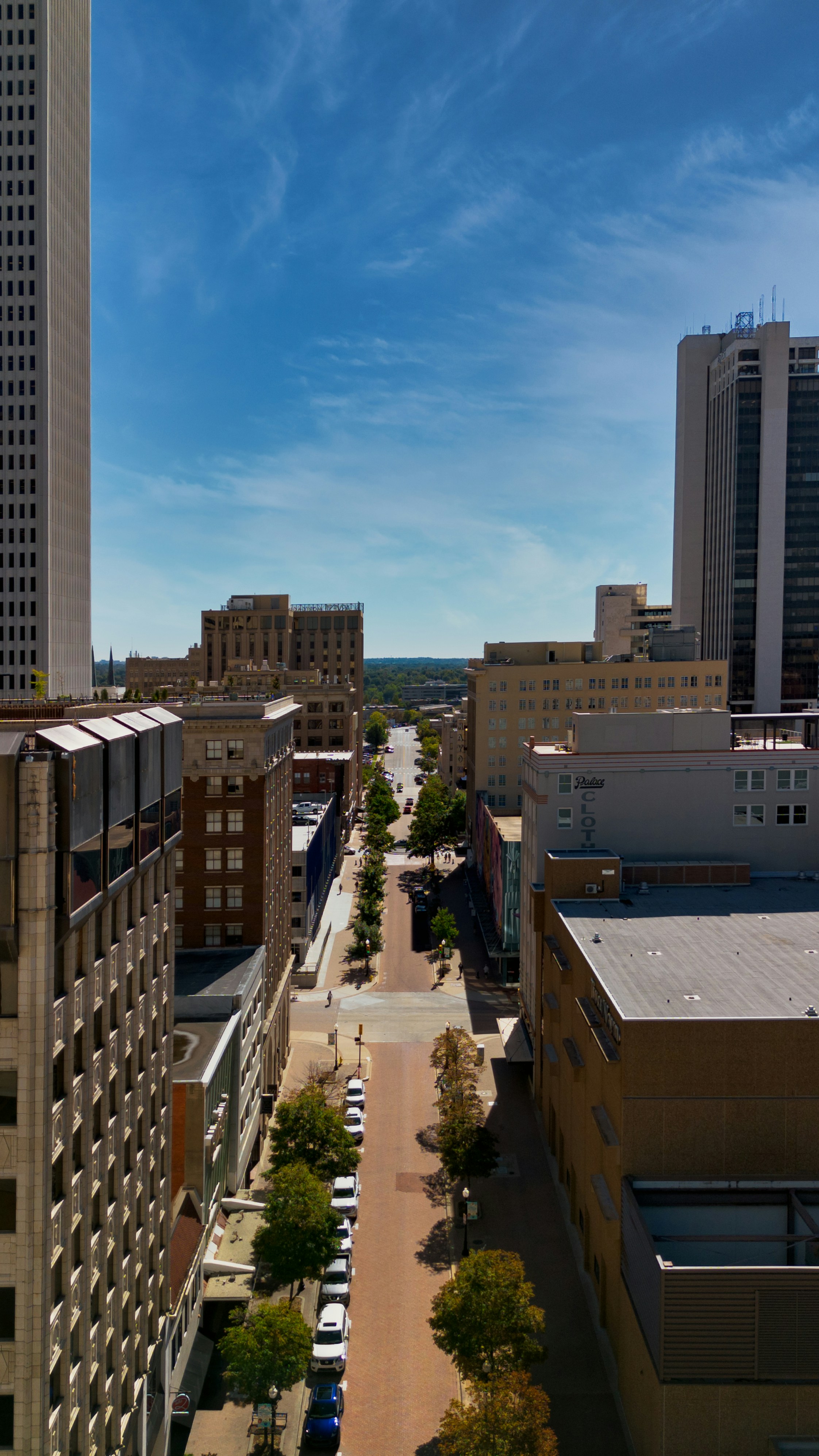 View down a city street lined with buildings and trees.
