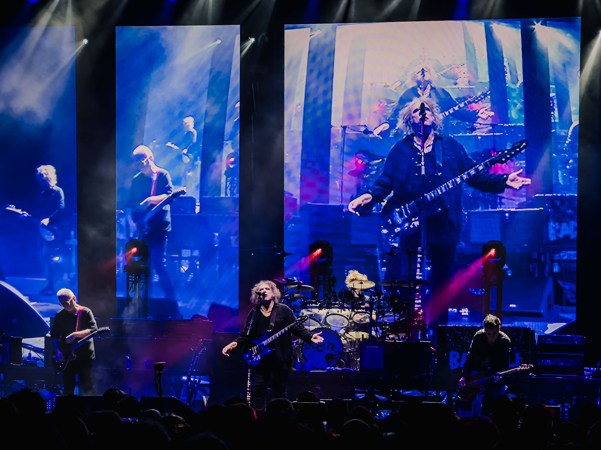 Montage à quatre écrans avec le bassiste au premier plan, concert de The Cure