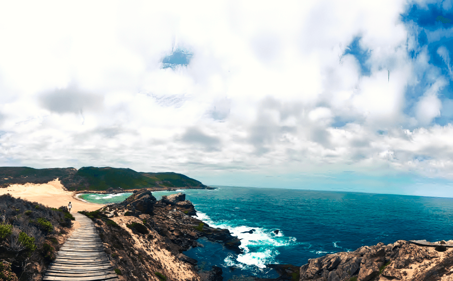 Woman practicing yoga in tree pose on a wooden deck overlooking misty mountain landscape at sunrise.