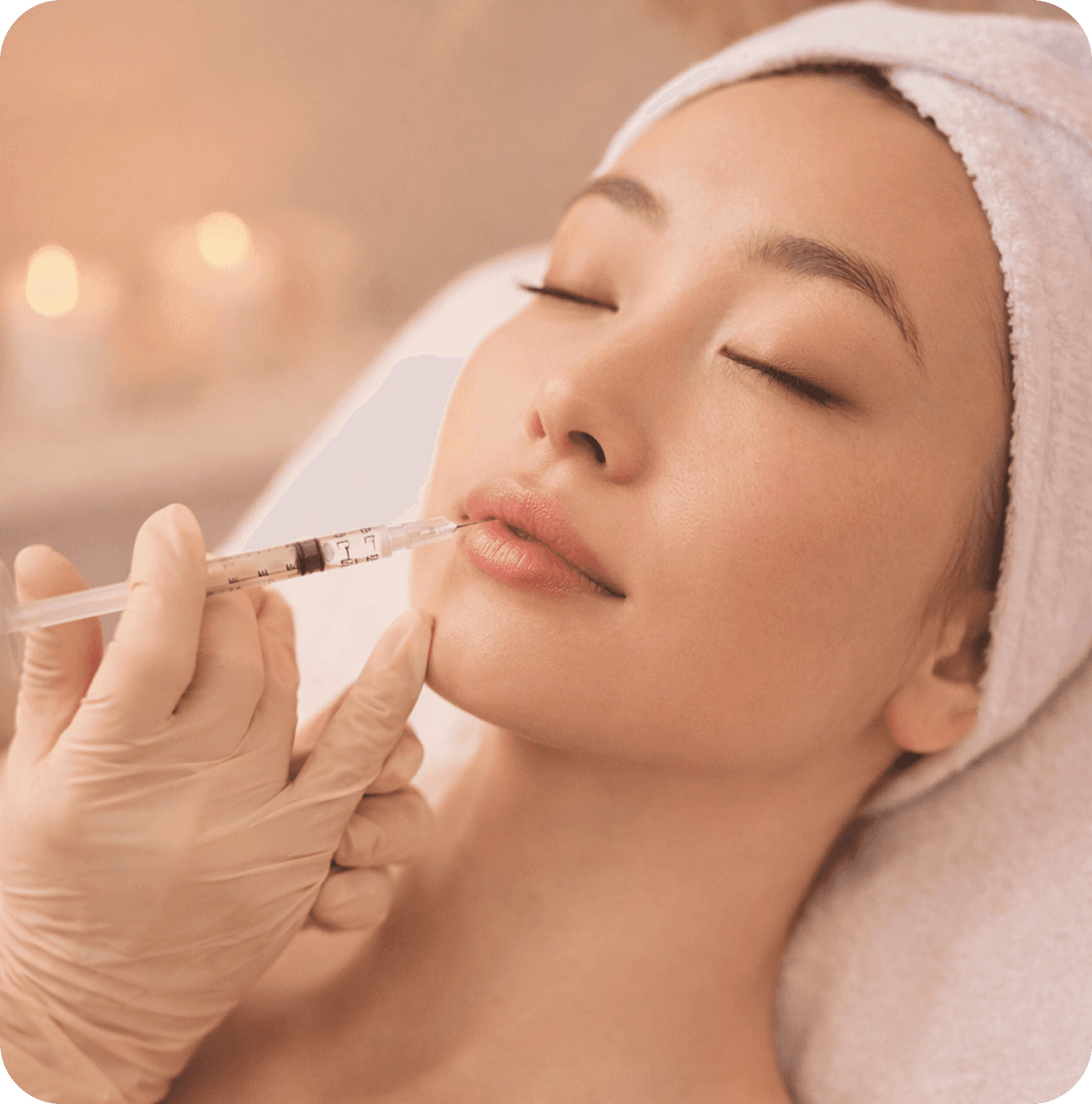 Woman in a towel applying pink under-eye gel patches while looking into a mirror on a vanity table