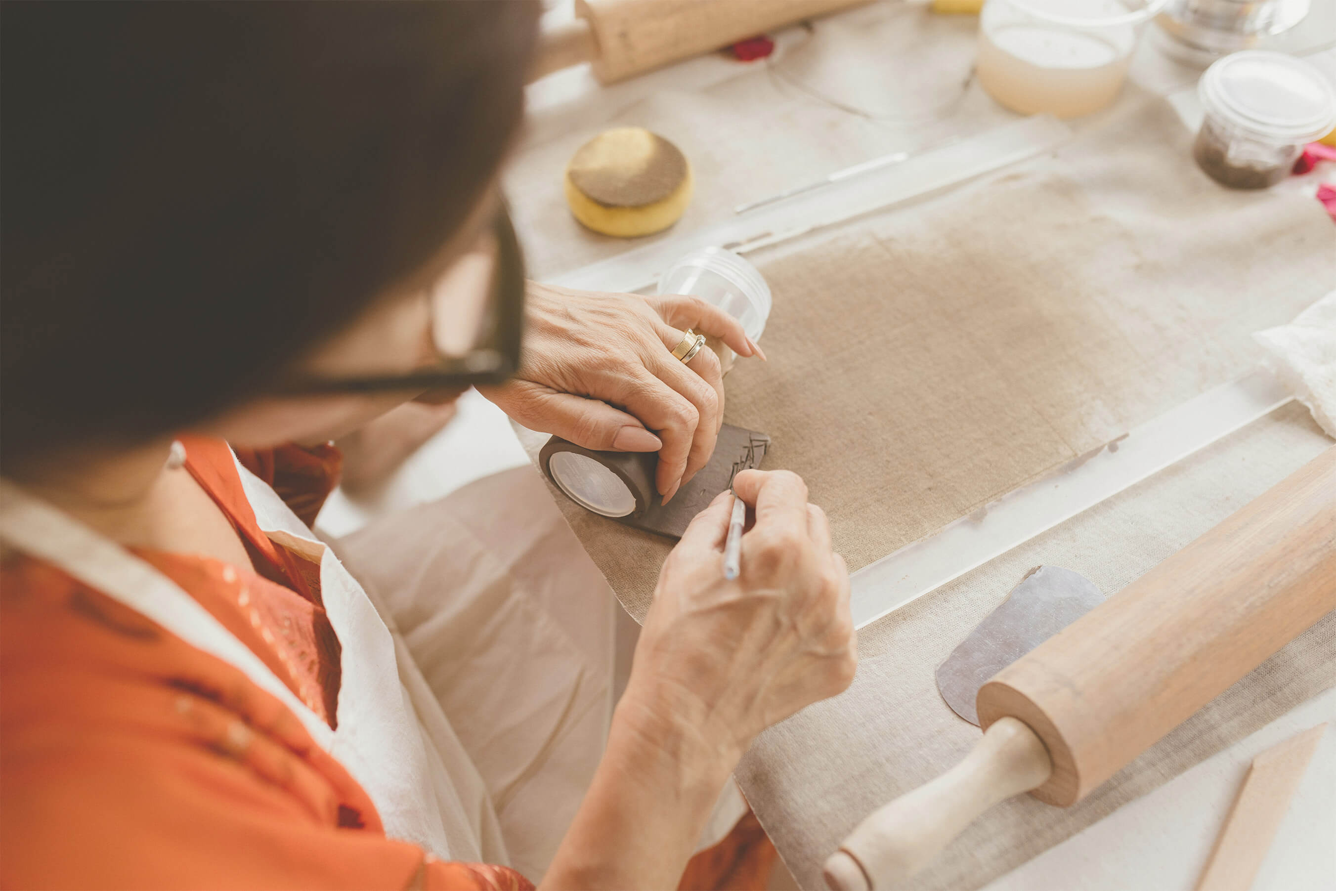 Hands scoring and shaping clay on a work table.