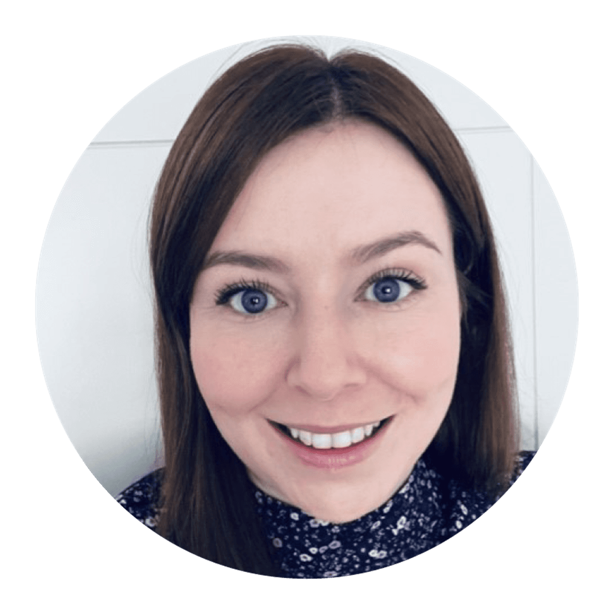 A circular portrait of a person with straight, dark shoulder‑length hair, wearing a patterned top, photographed against a neutral indoor backdrop.