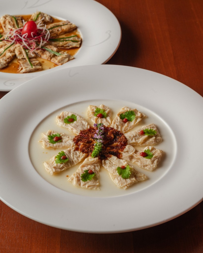 A beautifully plated dish featuring delicately arranged pieces of tofu or fish, garnished with vibrant herbs and colorful sauces, presented in a white plate.