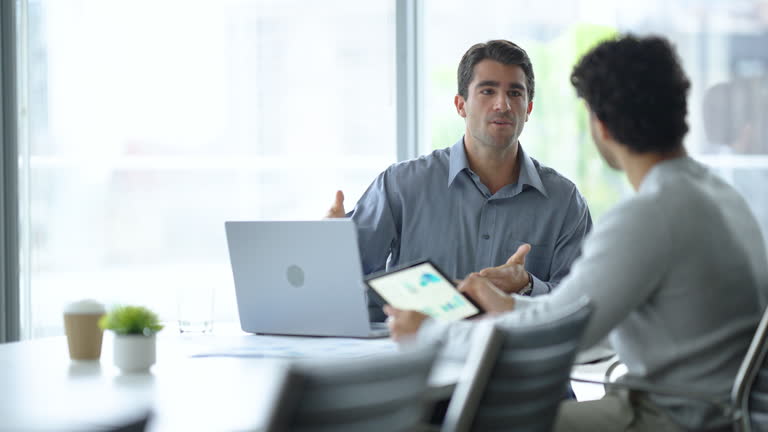 Three individuals gathered around a table, engaged in discussion while examining a laptop.