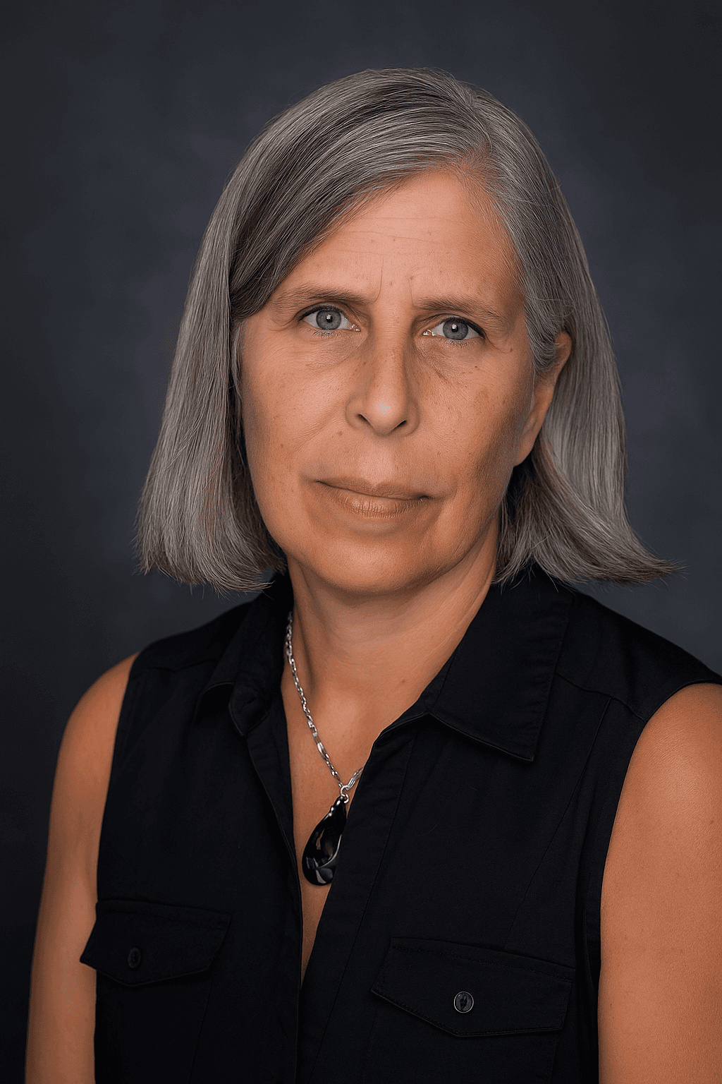Smiling female therapist with short gray hair, wearing a brown top and a purple shawl, surrounded by a cozy background.