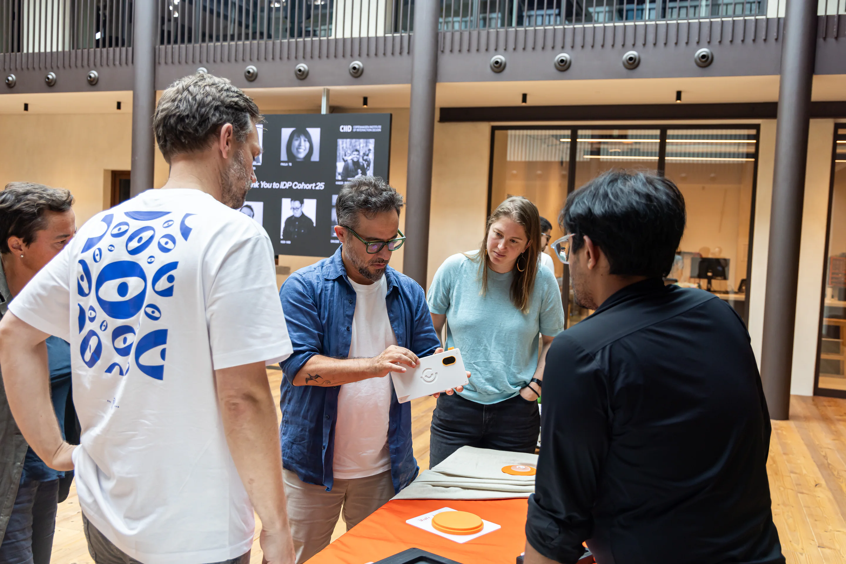 A group gathers around an exhibition table while one person holds the white camera prototype.