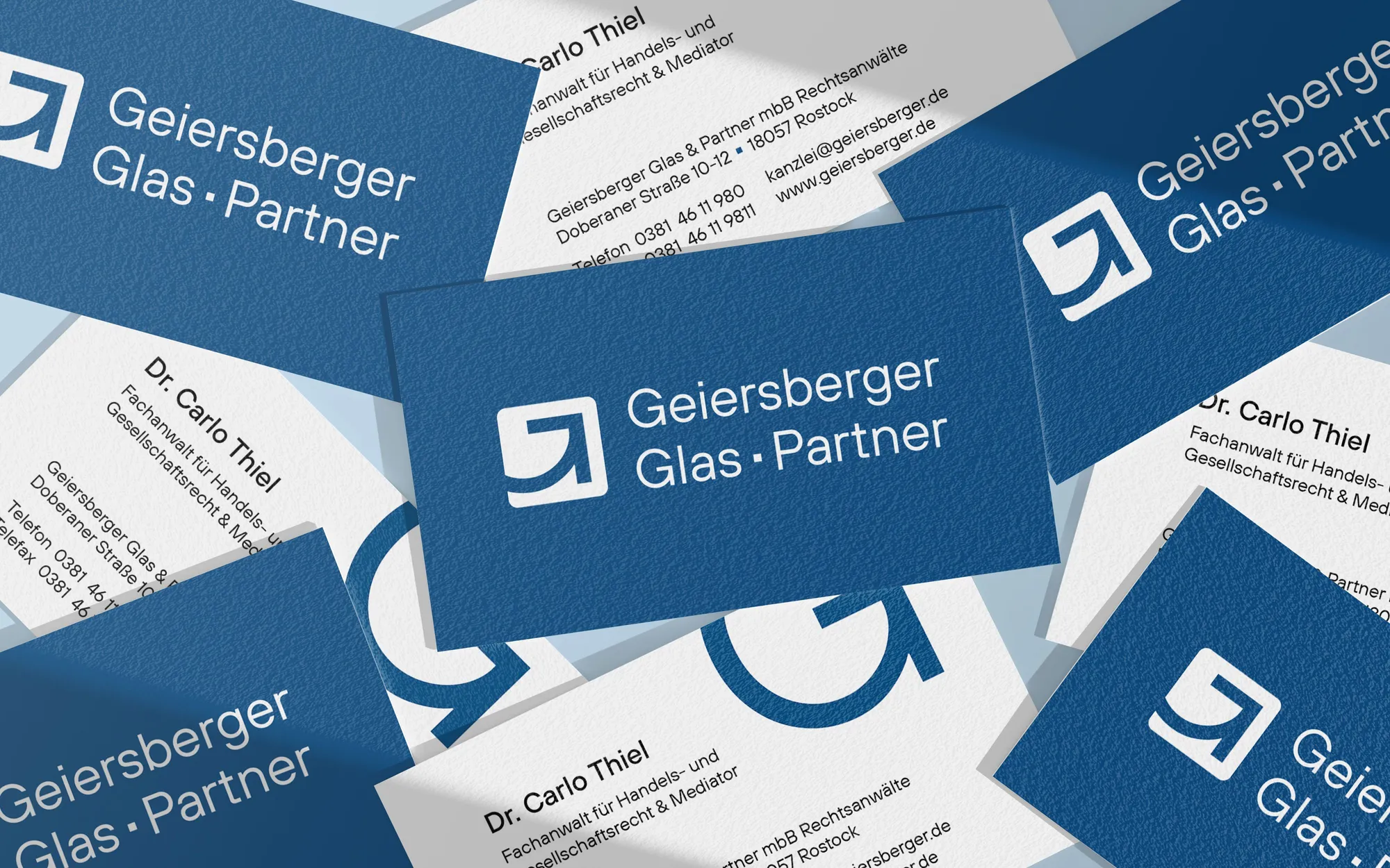 Mehrere blaue und weiße Visitenkarten von Geiersberger Glas & Partner auf blauem Untergrund.