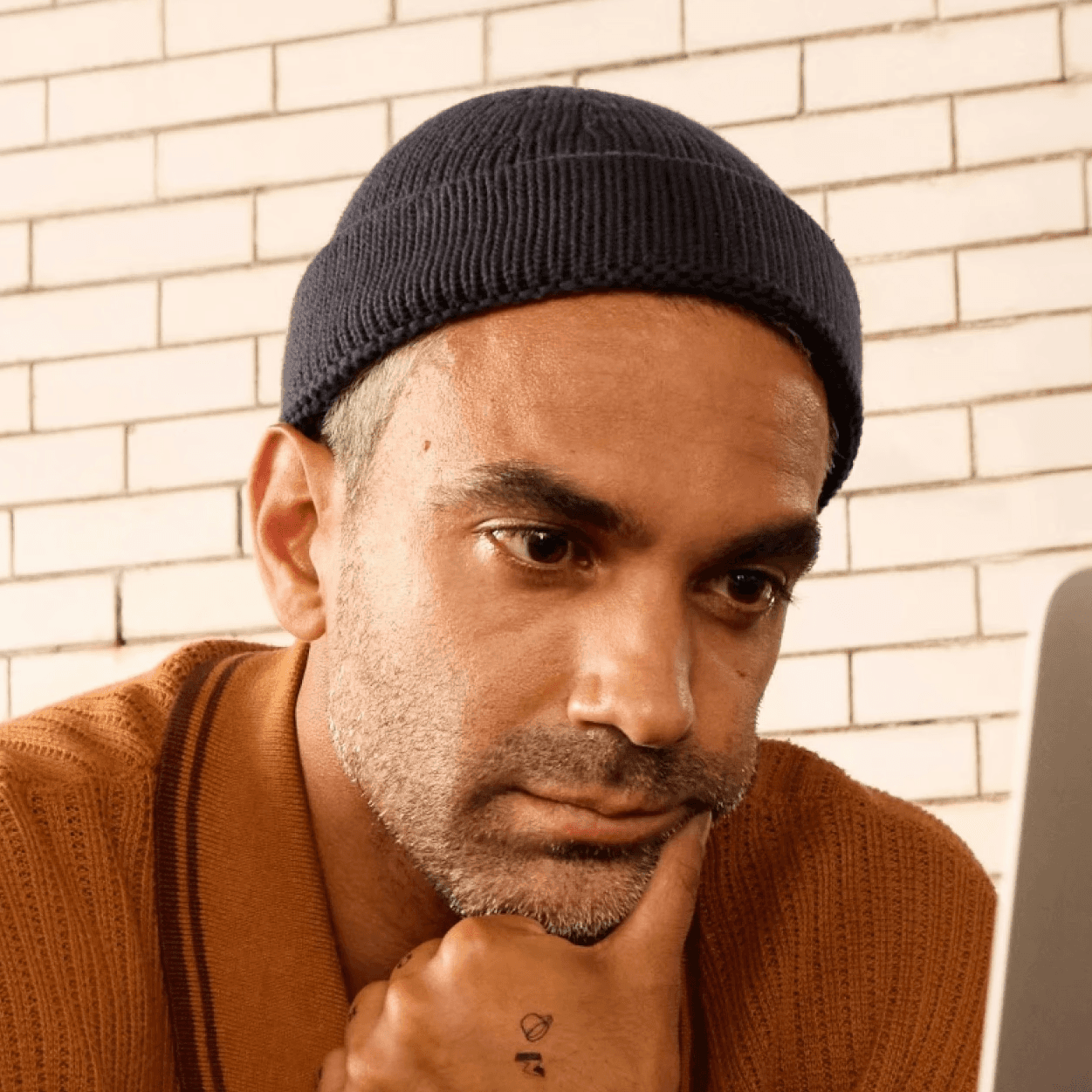 Man wearing a beanie and shirt works on a laptop.