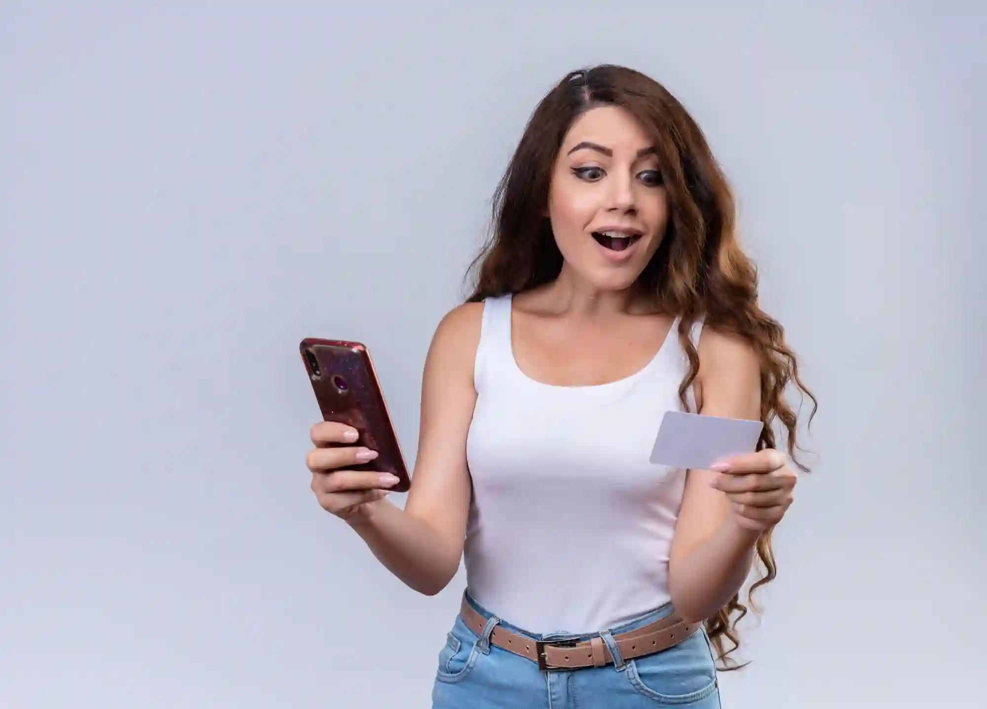 Surprised woman holding phone and credit card for online payment.