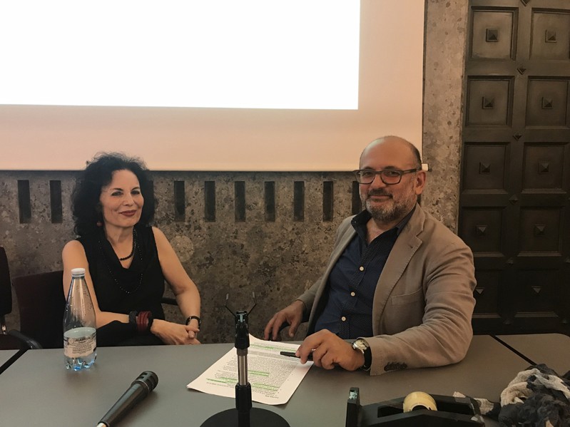 A photo of two people sitting at a desk in front of a projector screen.