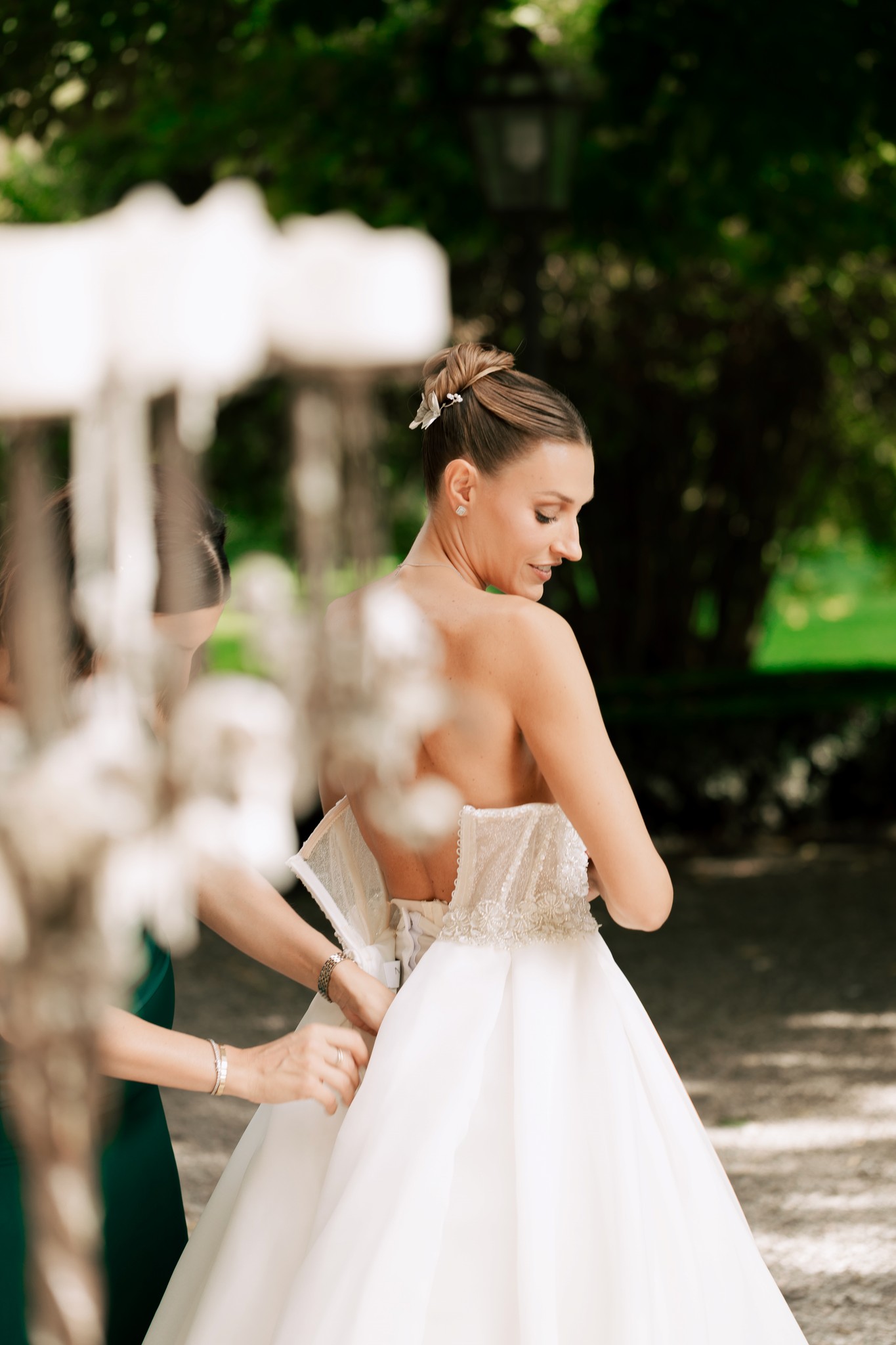 Sposa in abito bianco nei preparativi al ricevimento, aiutata nella vestizione nel parco di Villa Ferrari