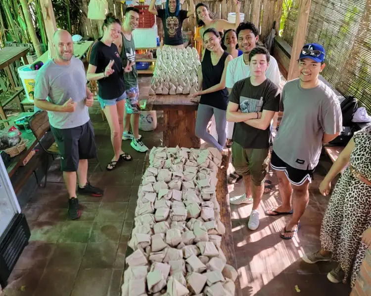 Group of volunteers standing behind rows of packaged meals ready to be delivered to families.