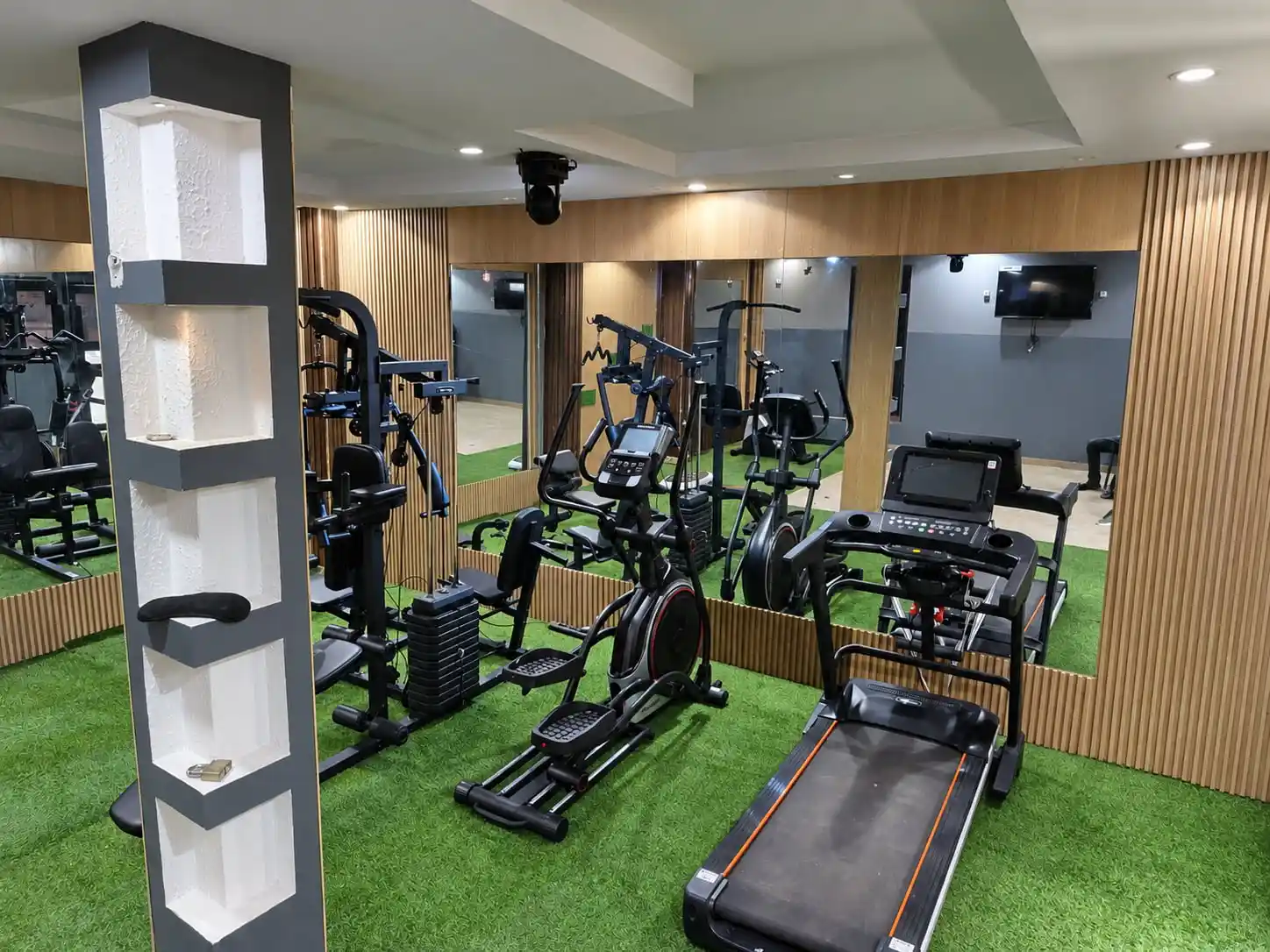 Salle de sport avec tapis de course, vélo elliptique et appareils de musculation devant des miroirs.