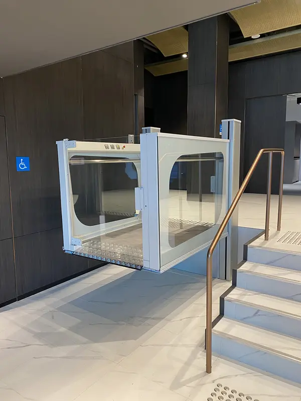 Hublift mit Glaskabine neben einer Treppe in einem öffentlichen Gebäude