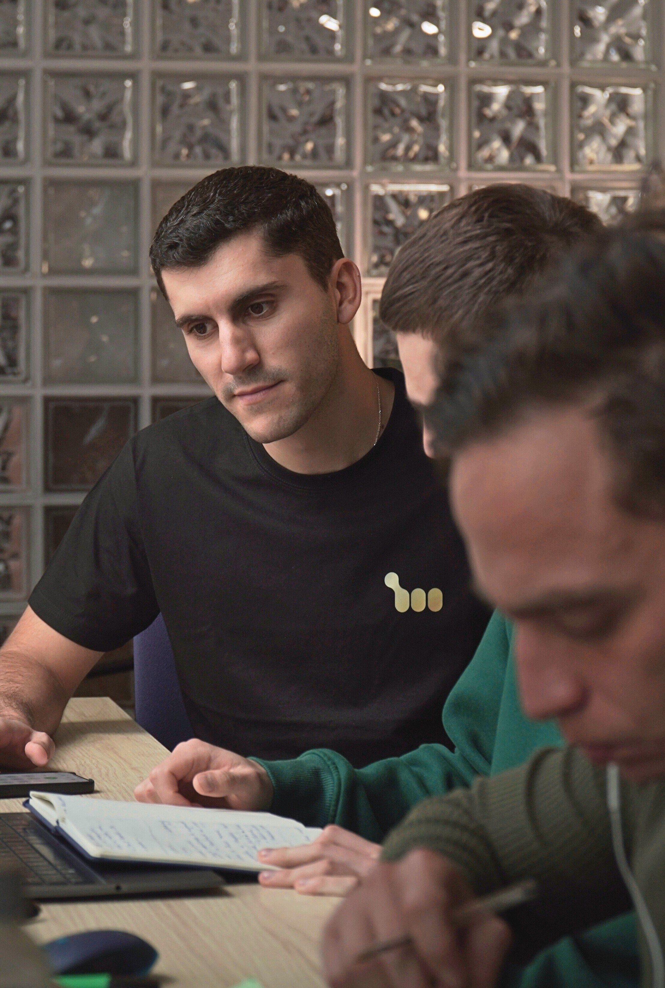 A smiling woman with her arms crossed, standing against a dark green background. She has long, dark hair.