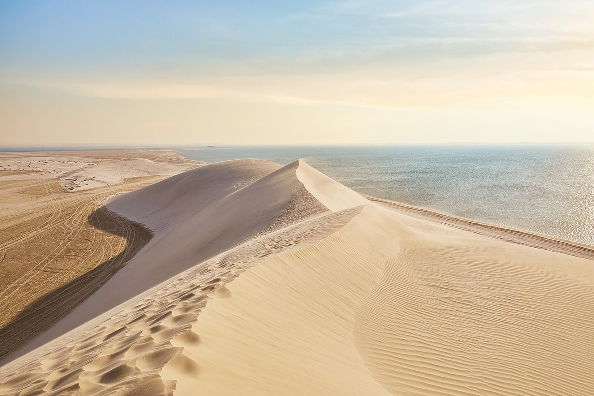 Une crête de dune qui plonge dans la mer turquoise de Khor Al Adaid, la mer intérieure du Qatar, sous un ciel clair, une sortie qui redevient possible en plein jour après le 20 septembre