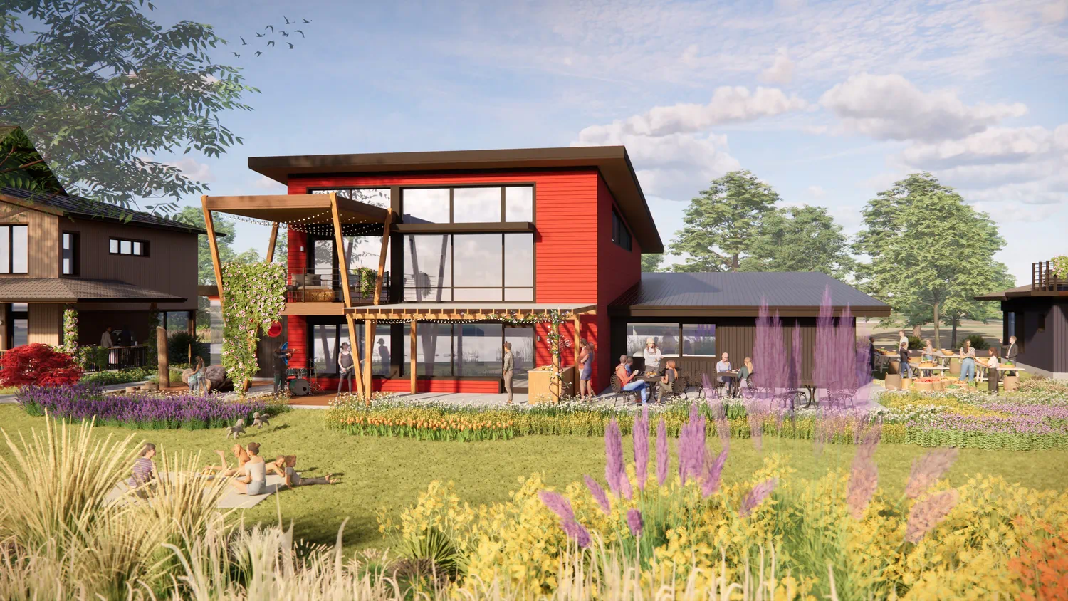 Red community commons building with large windows and covered patio, where neighbors gather at outdoor tables amid gardens and open green space.