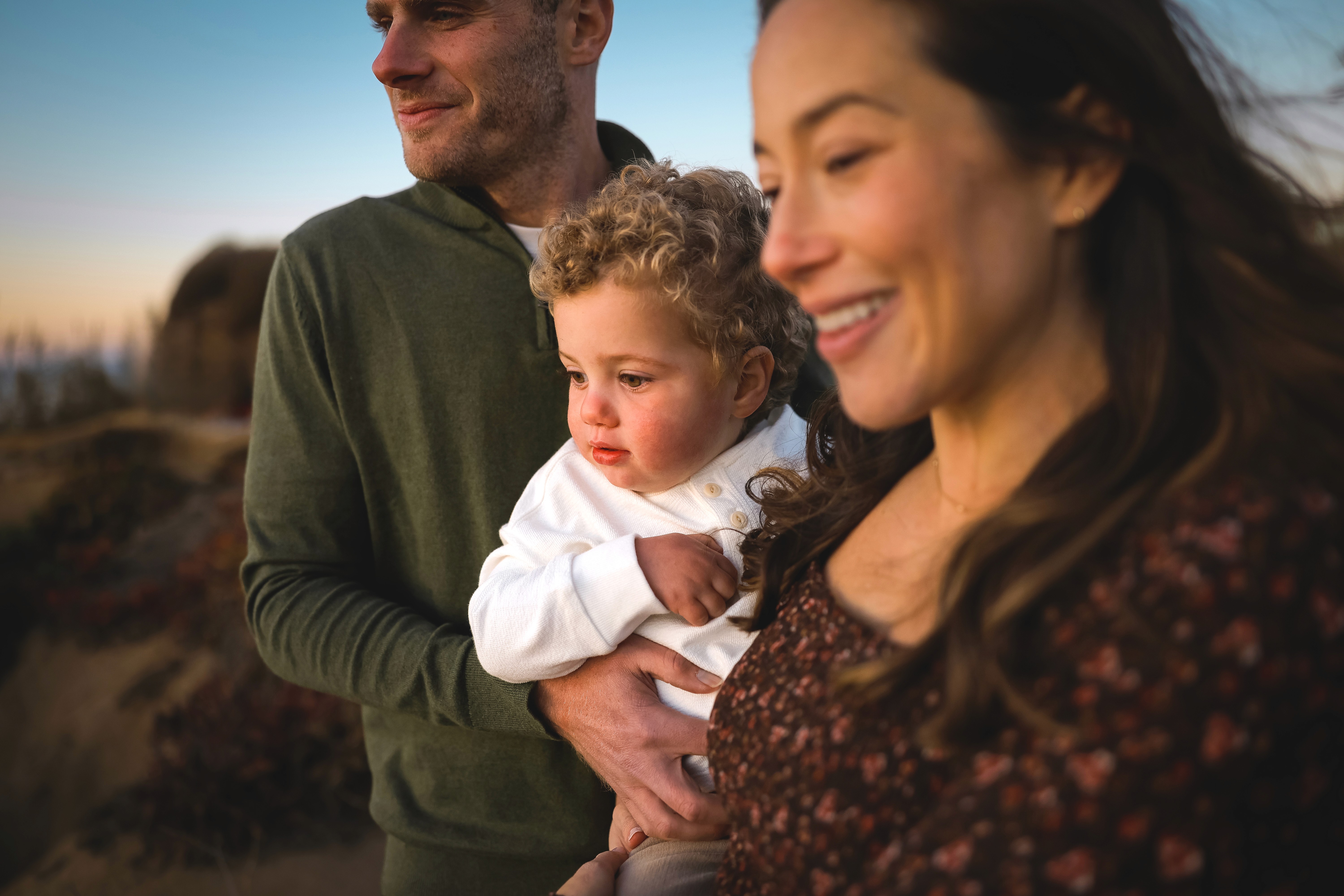 Smiling toddler being held by parents during a family maternity session.