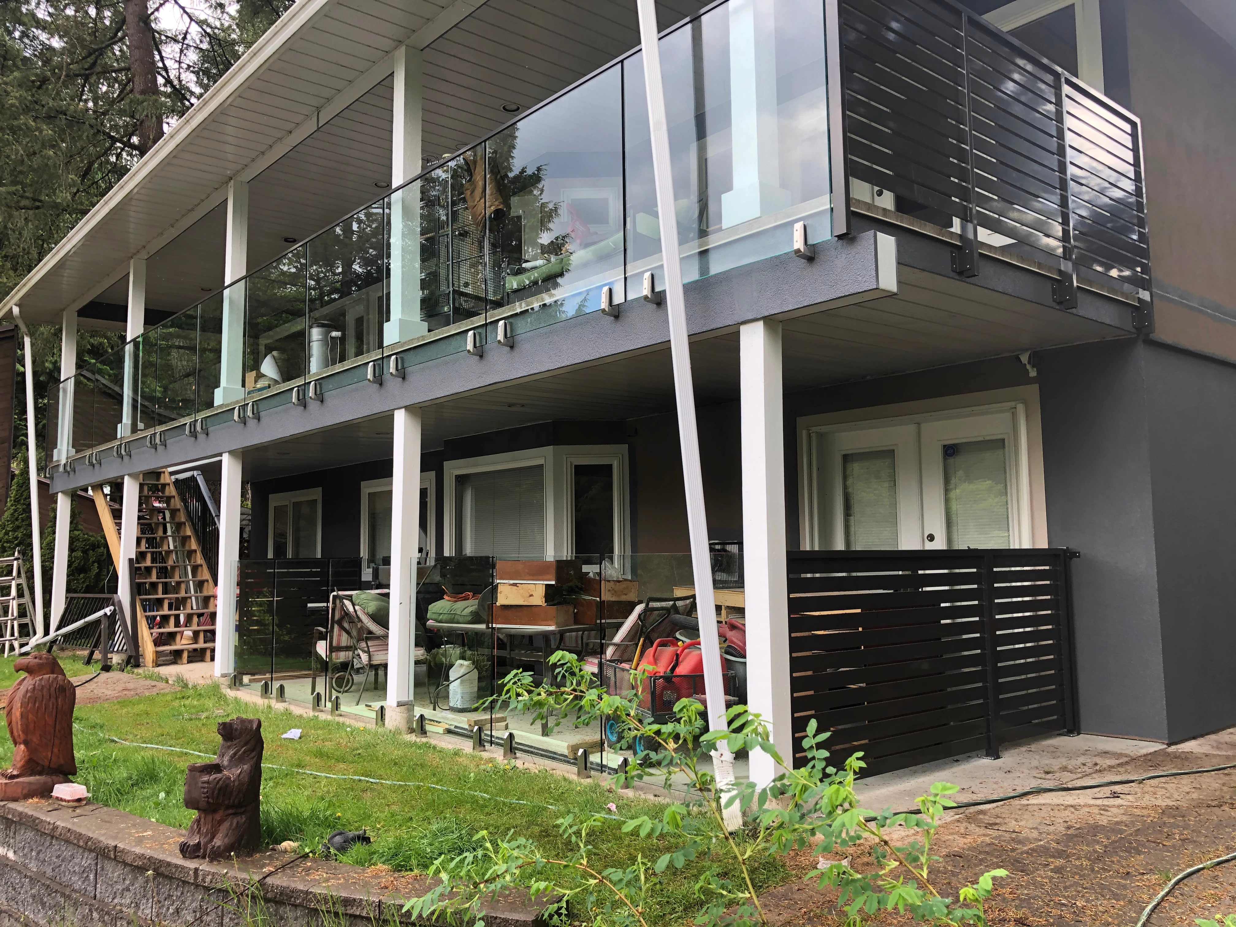 Frameless glass guardrail on an elevated deck above a glass privacy fence at a forested BC coastal home.