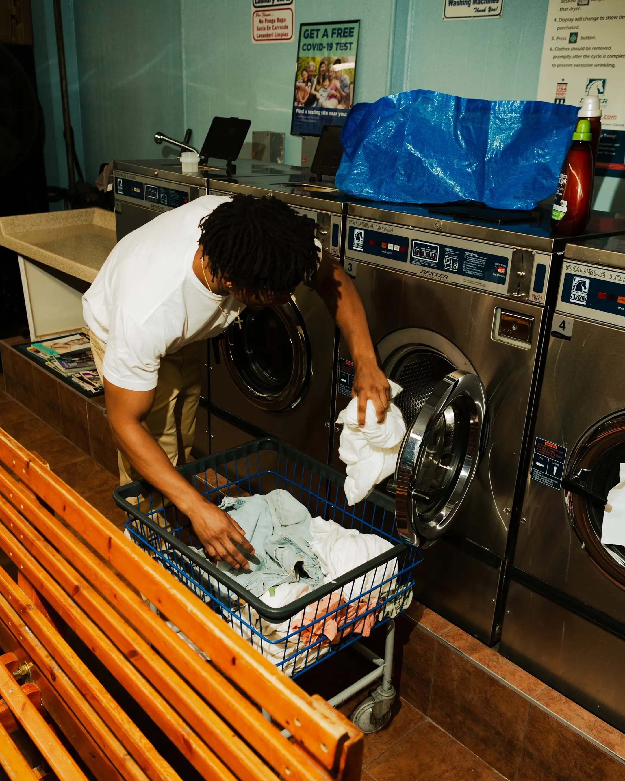 Laundromat attendant loading clothes from a wire basket cart into a commercial washing machine.