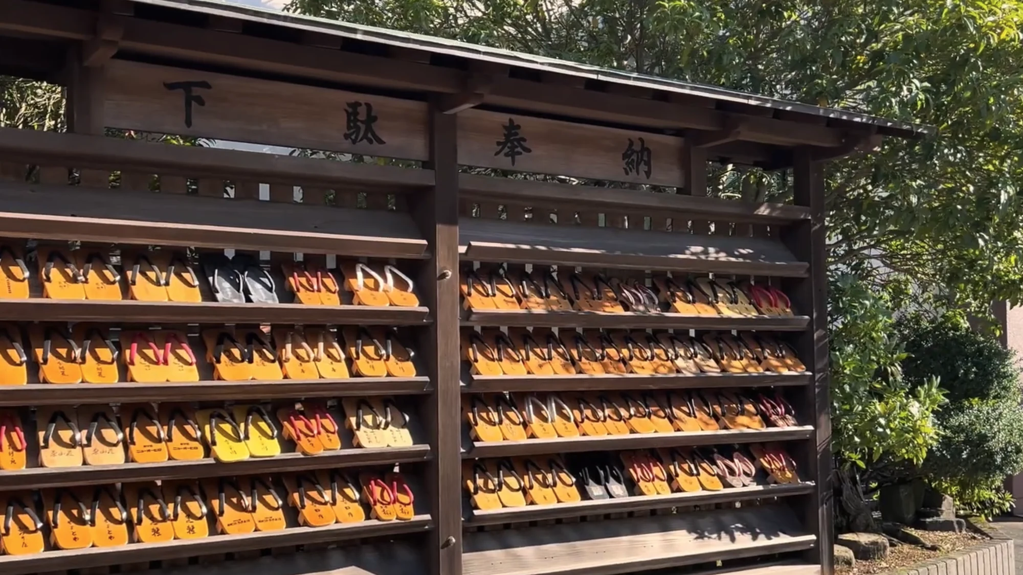 Rows of wooden geta on timber racks under a carved sign at a Kinosaki bathhouse.