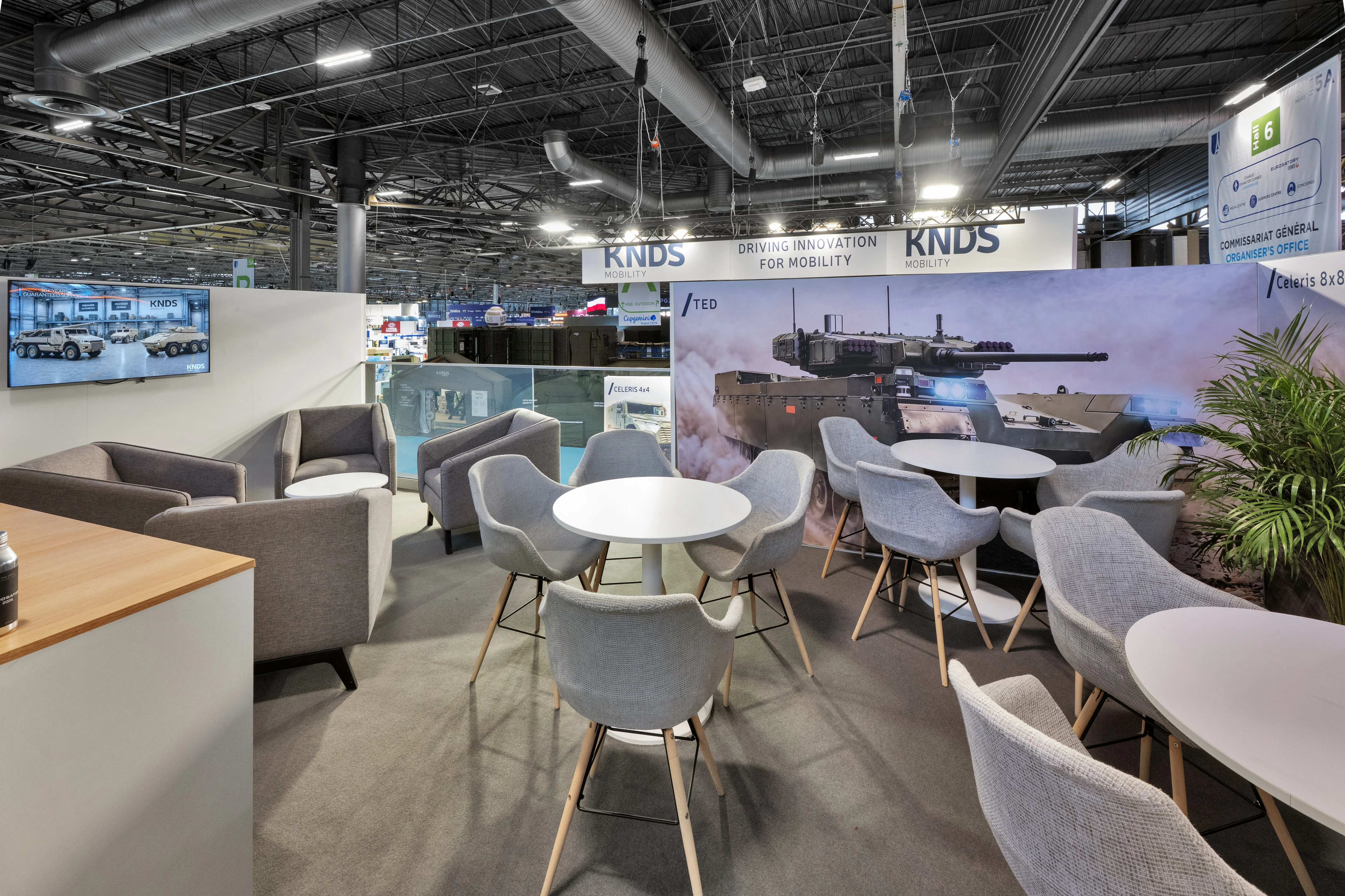 Stand KNDS Mobility conçu et réalisé par Expace à Eurosatory 2026 – espace sur-mesure défense avec blindé SCATA, châssis Celeris écorché, bandeau suspendu « Driving Innovation for Mobility » et lounge à l'étage.