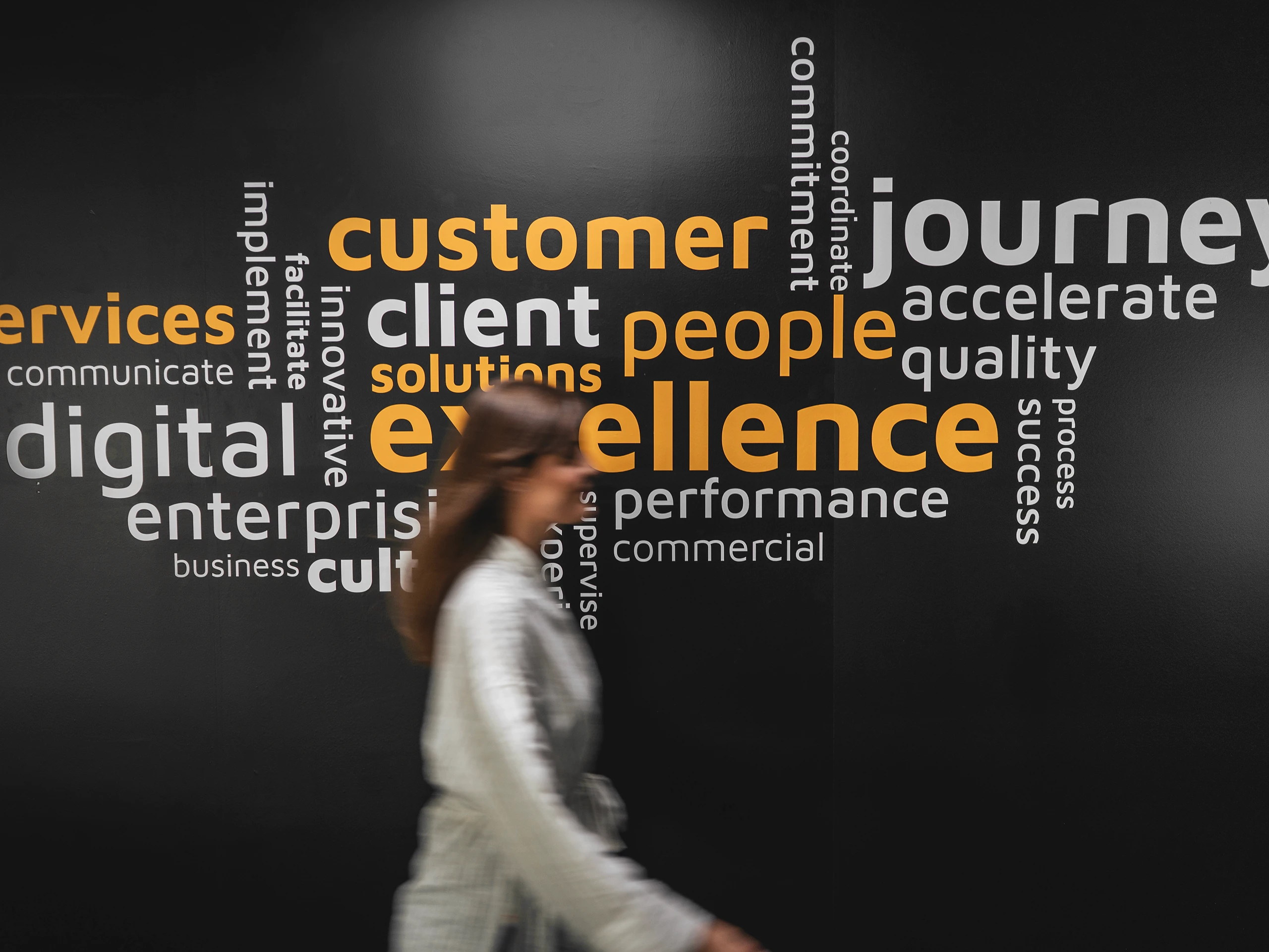 Office wall with business value keywords and a person walking past.