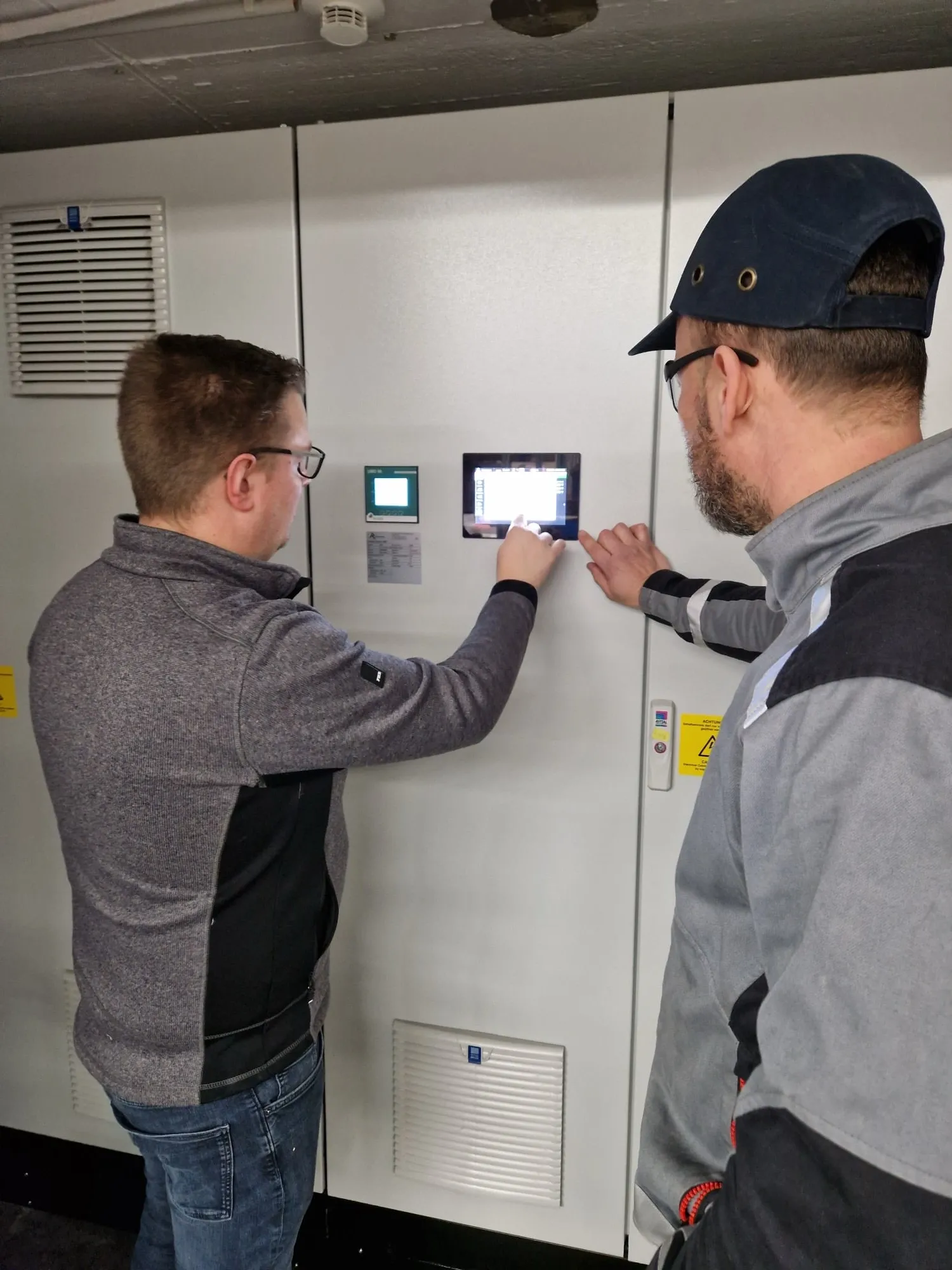 Zwei Fachleute stellen Einstellungen am digitalen Bedienfeld in einer industriellen Arbeitsumgebung ein.