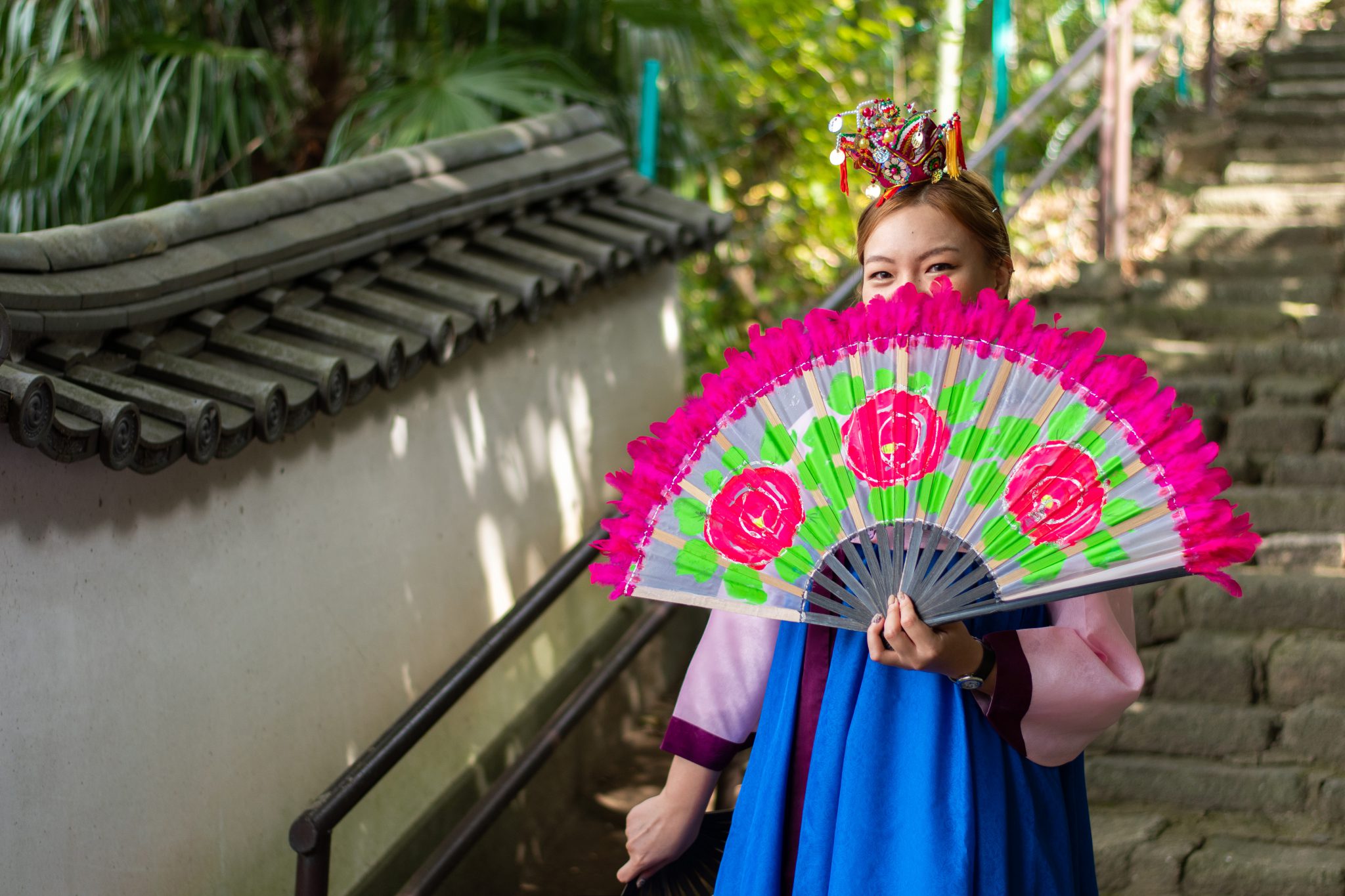 Young woman wearing Korean clothing, holding a large pink and green fan