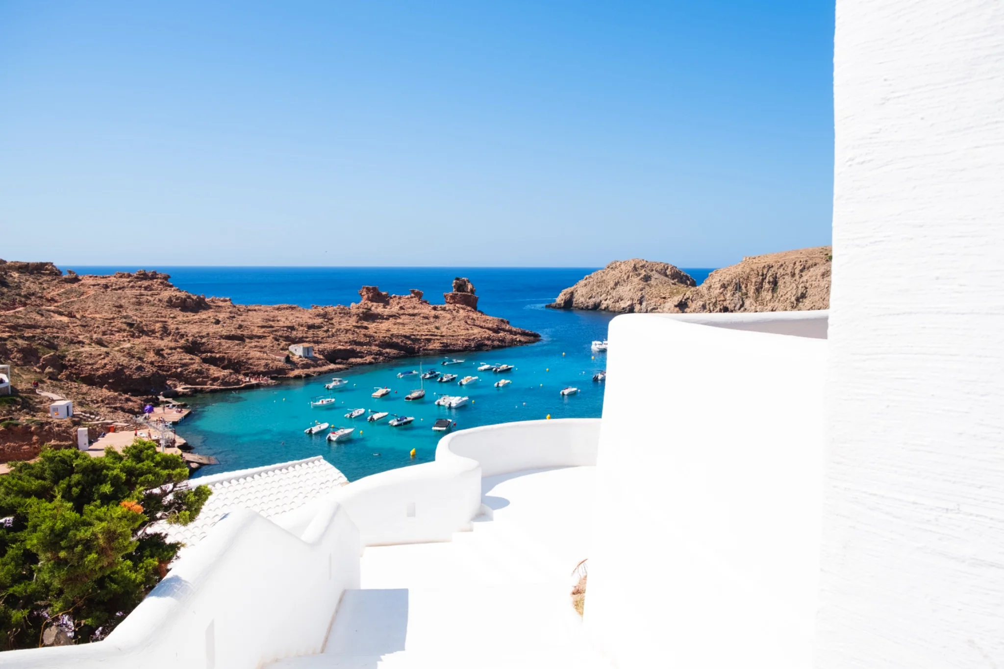 Hidden Mediterranean cove in Mallorca with turquoise waters, traditional white architecture and boats, discovered on a private tailor-made island experience.