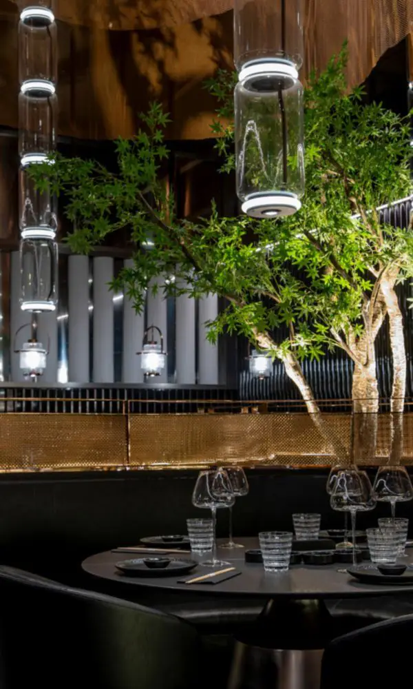 Tables rondes dressées au pied d’un arbre éclairé, au cœur de la salle