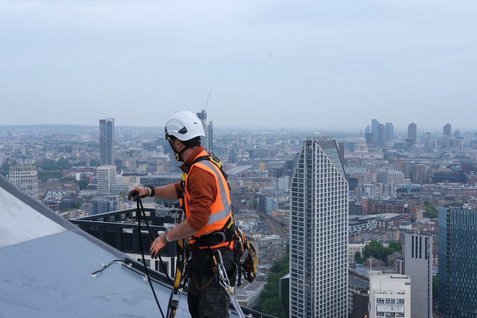 Rope-access technician preparing equipment on a rooftop above London