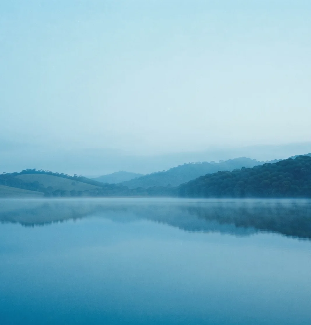 Represa na hora azul, com névoa sobre a água e as montanhas ao fundo.