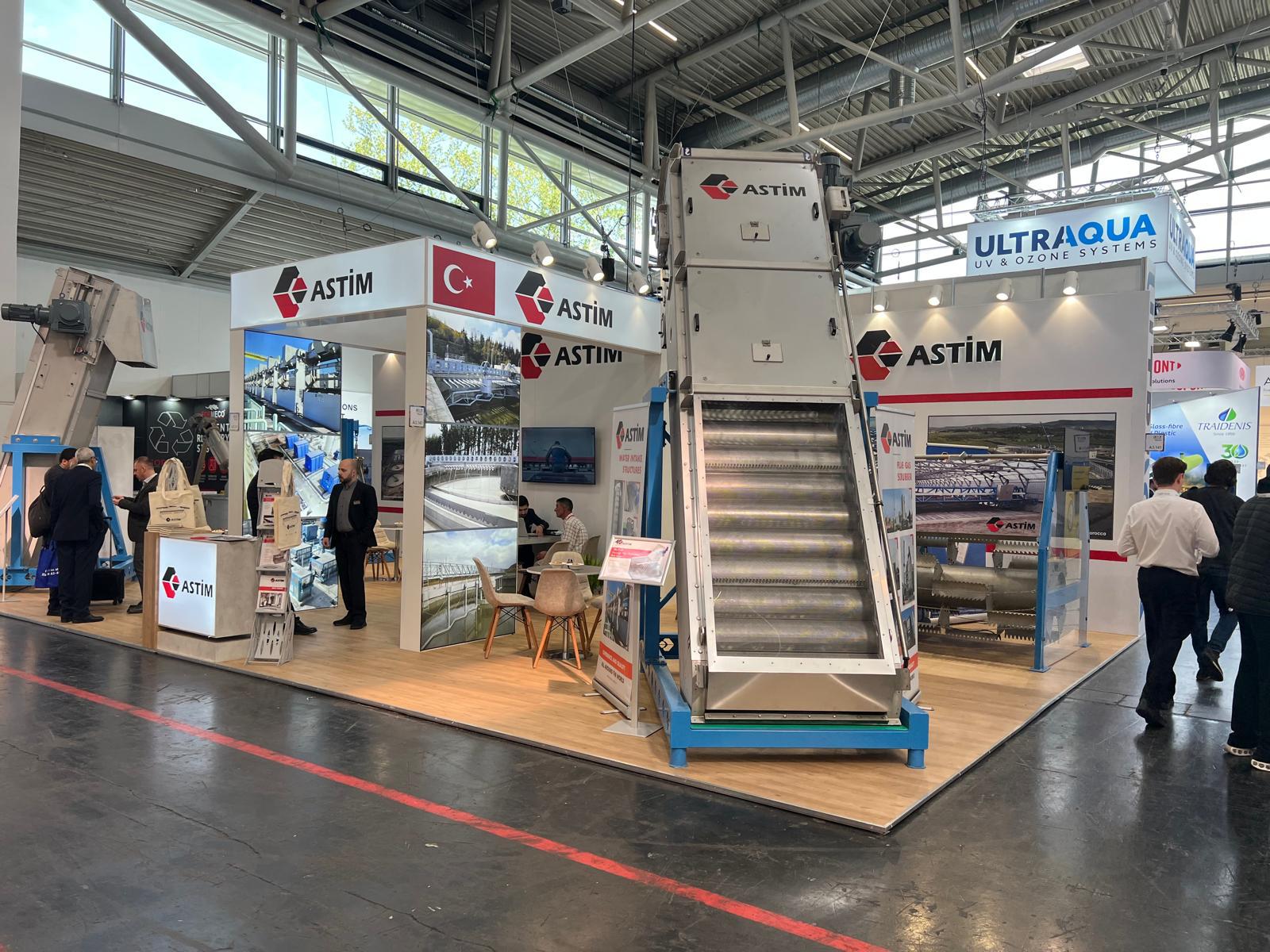 ASTIM exhibition stand at IFAT 2026 Munich, featuring large industrial machine displays and graphic panels.