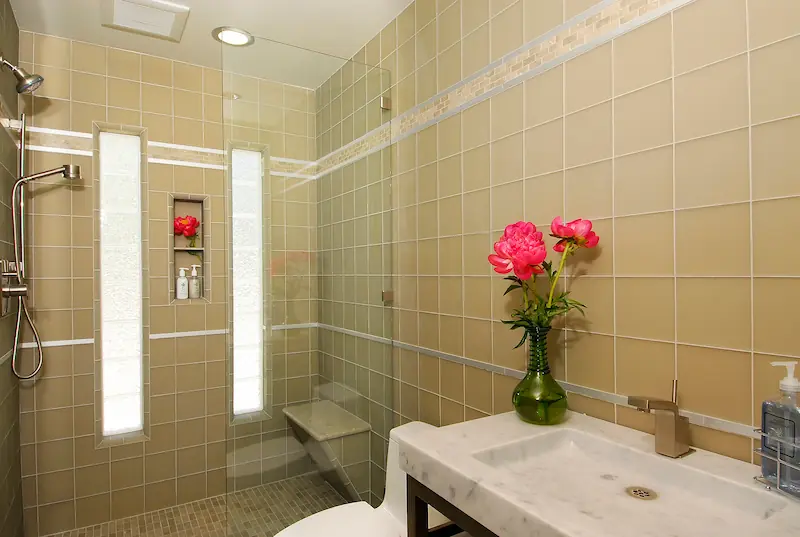 Tiled bathroom with glass shower, white basin, and pink flowers in Irvine Transitional Modern. Photo by Chris Darnall.