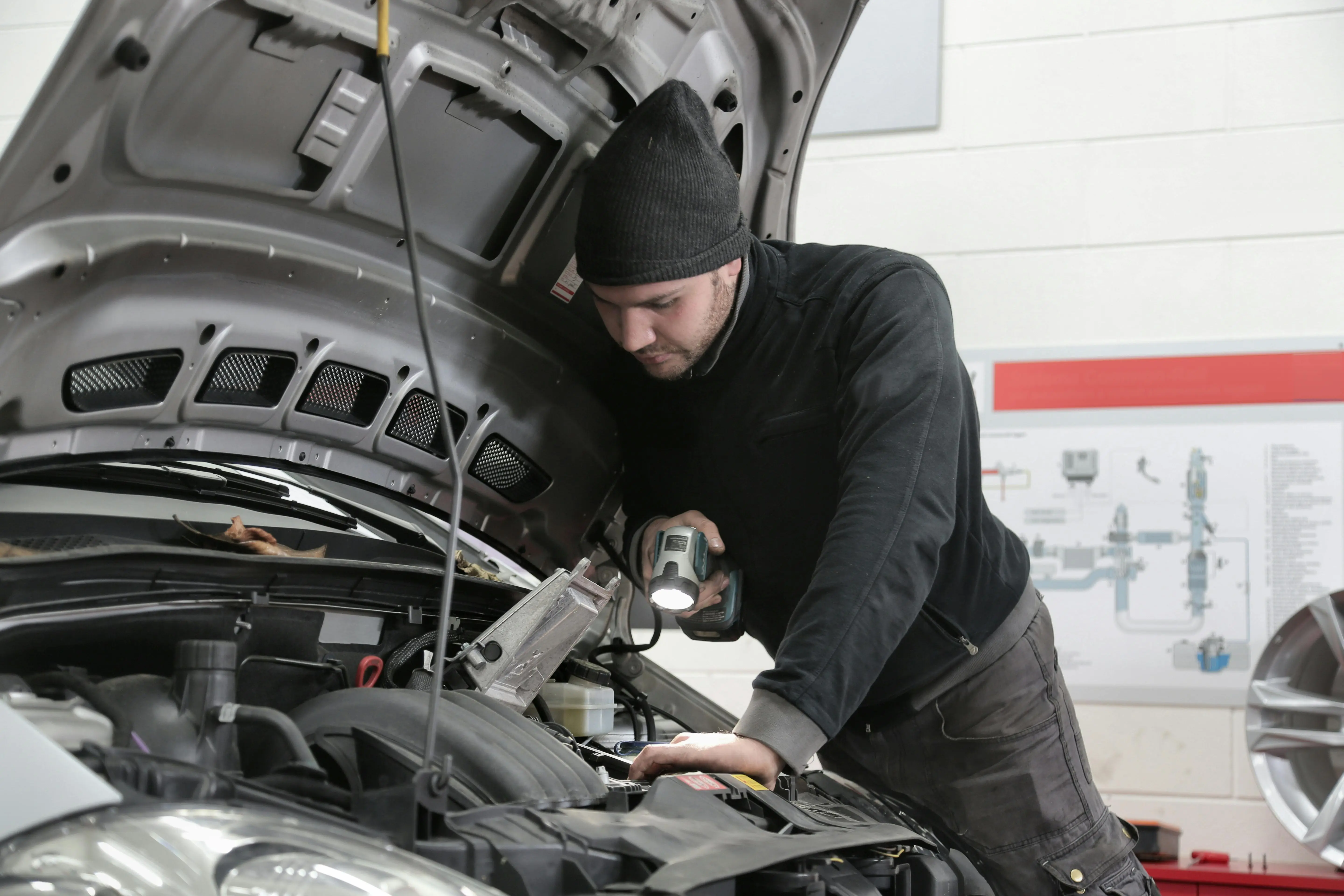 Un professionnel AutoJust inspecte le moteur d’un véhicule avec une lampe, illustrant la précision des contrôles physiques sur le terrain.