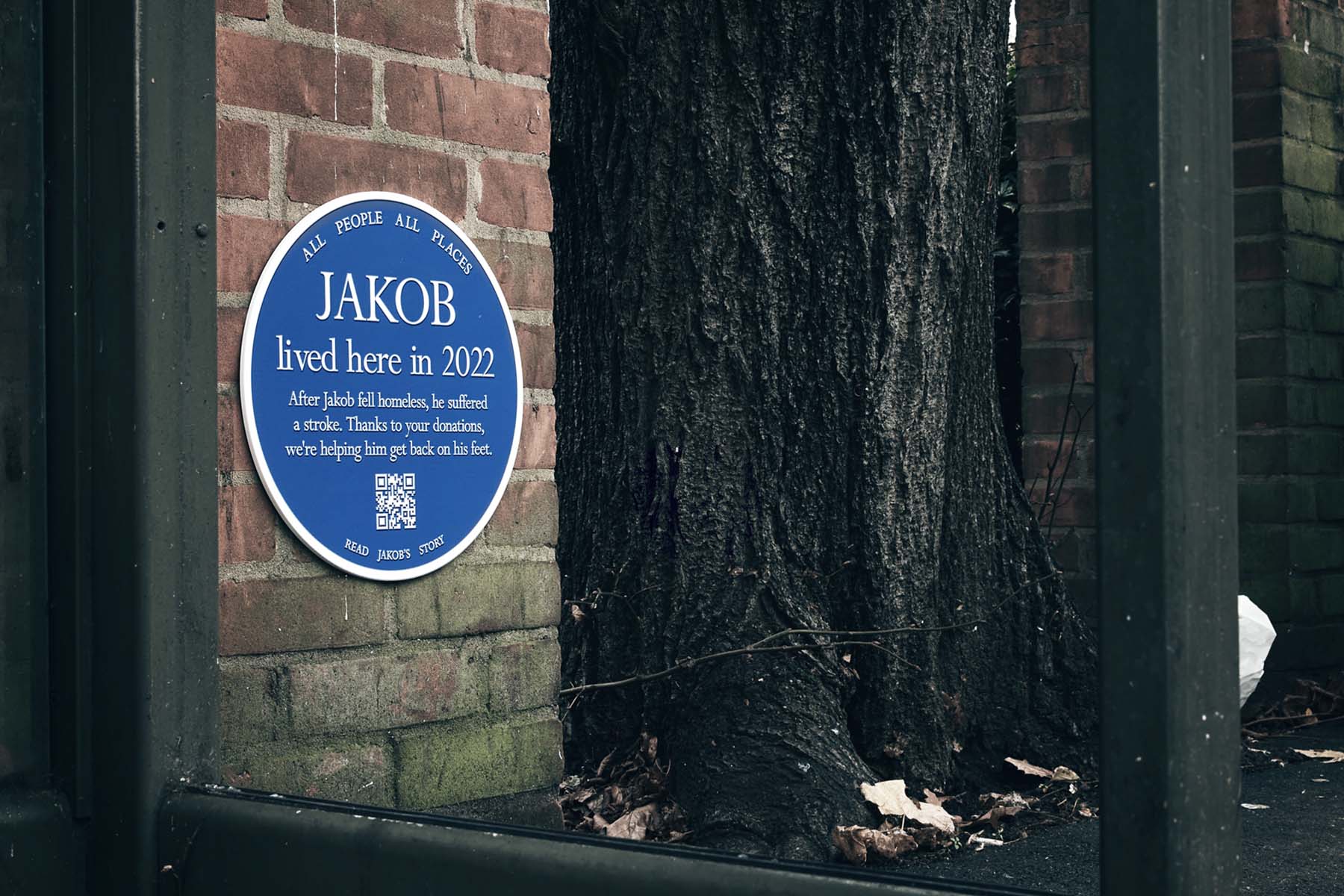 Blue plaque attached to a brick wall by a bust stop outside that say's Jakob lived here in 2022