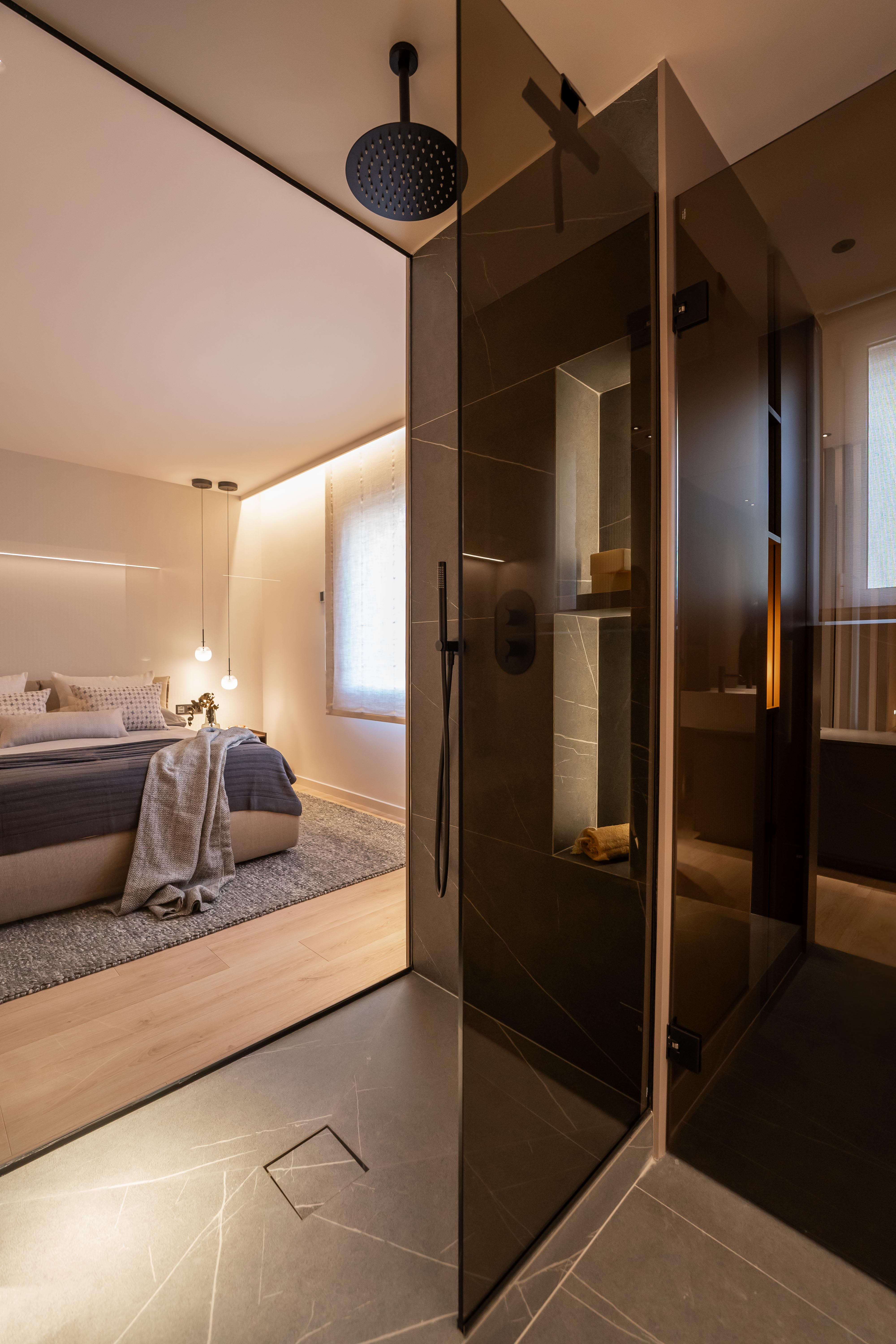 Dormitorio minimalista con tonos grises visto desde cristal del baño en suite