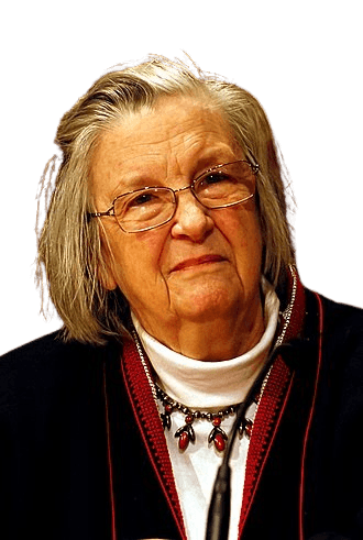 An older woman with gray hair and glasses, wearing a white turtleneck, dark jacket with red trim, and a distinctive necklace, is pictured in an indoor setting. Her thoughtful expression and formal attire suggest wisdom and experience, creating a warm and intellectual atmosphere.