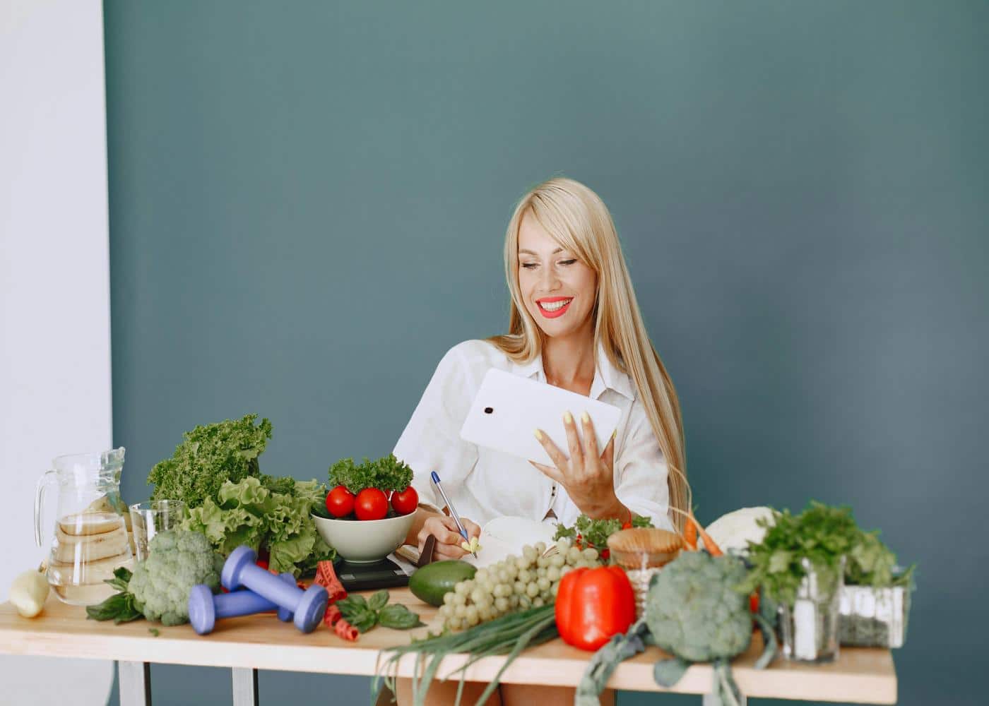 Woman sitting at table full of veggies on tablet and taking notes