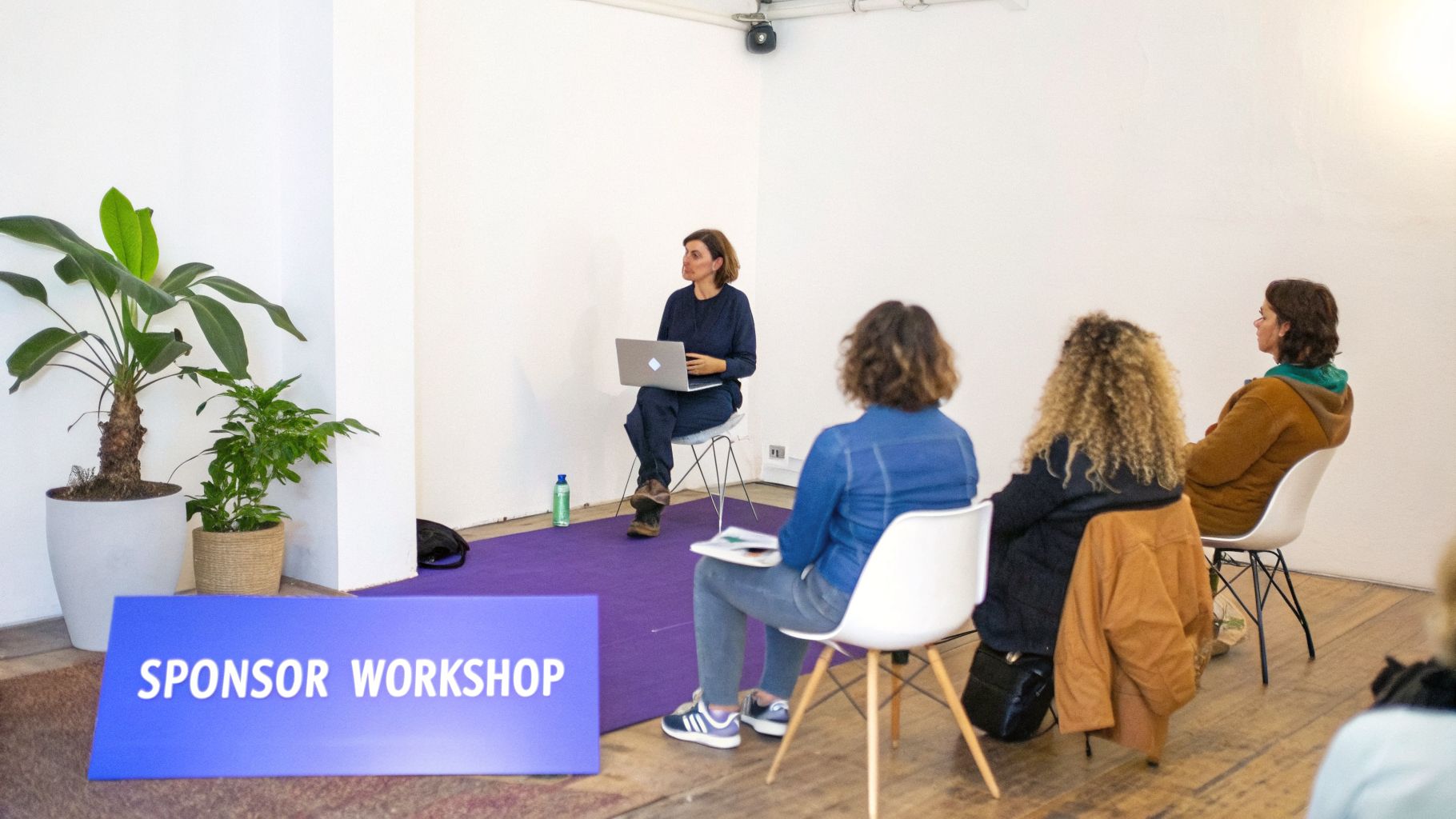 A woman leads a sponsor workshop, presenting from a laptop to a small audience in a bright room.
