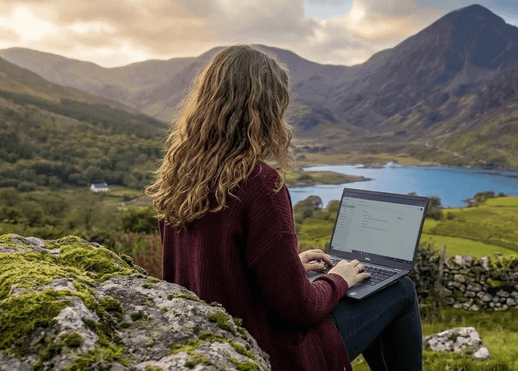Web designer Yosta working on a laptop while overlooking a mountain lake in Kenmare, Ireland, representing the high-capacity 'Commercial Plaza' e-commerce package.
