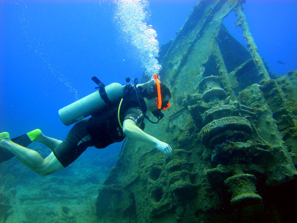 Diver examining coral-encrusted machinery on the hull of a shipwreck