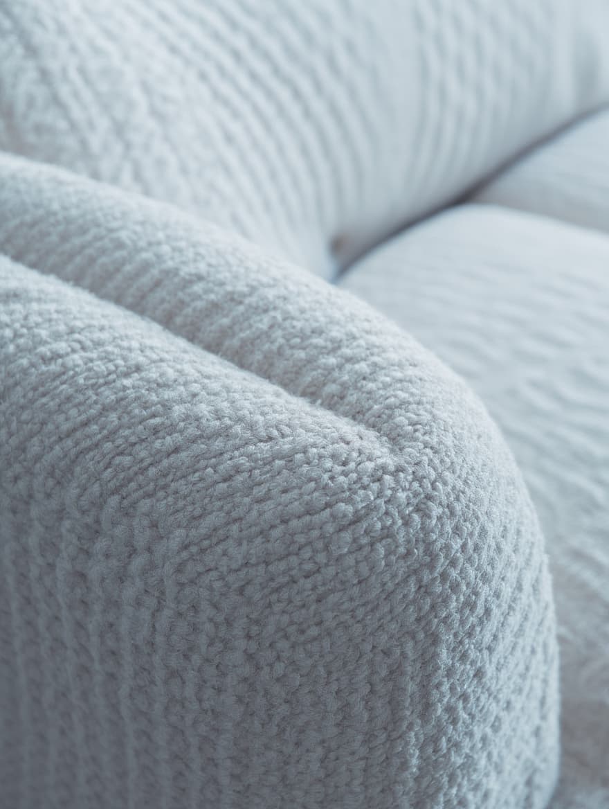 Close-up image of a light gray, textured fabric sofa cushion with a soft, woven pattern, highlighting the plush and comfortable material.