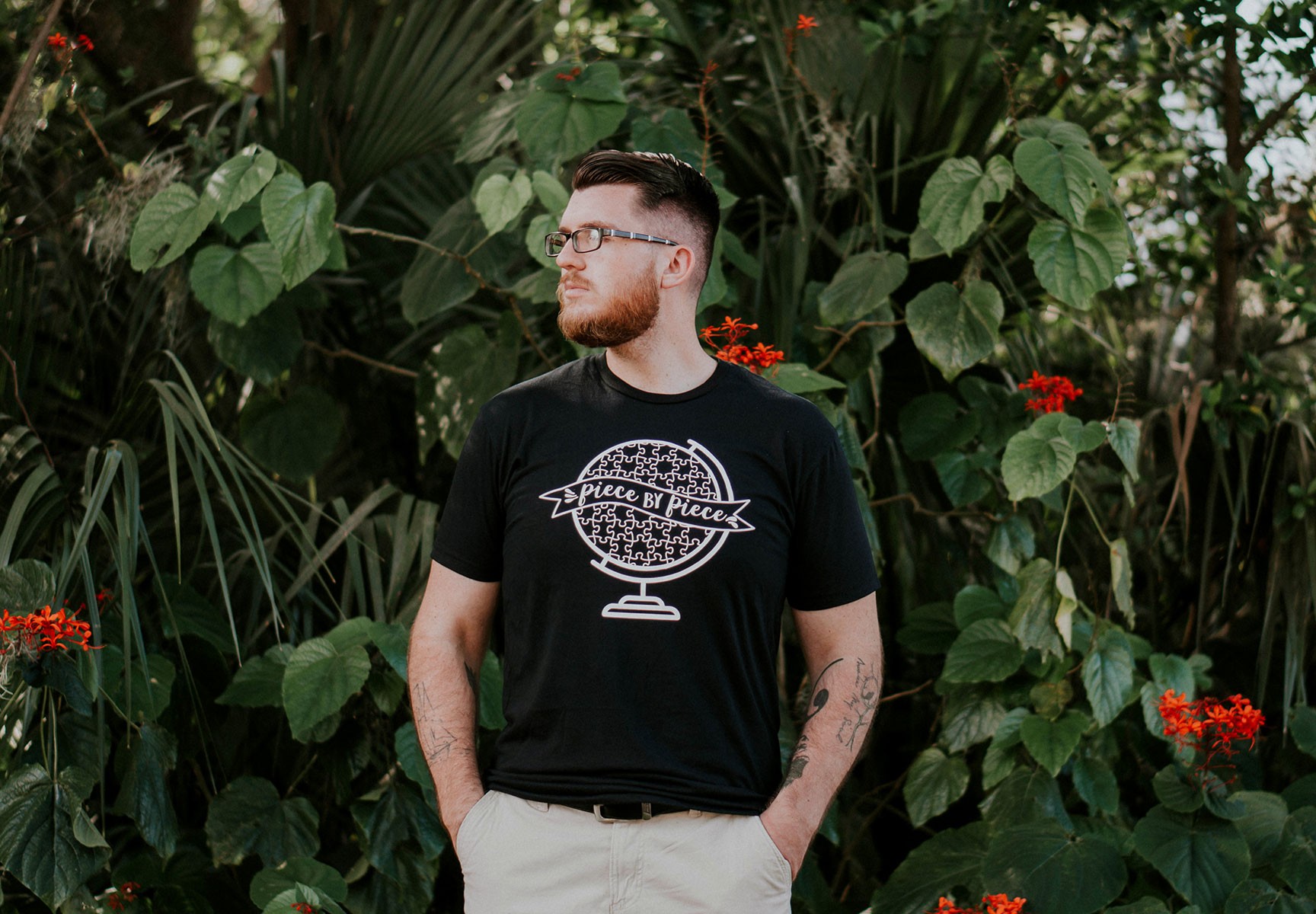 Man in black t-shirt with globe design standing in lush green garden.