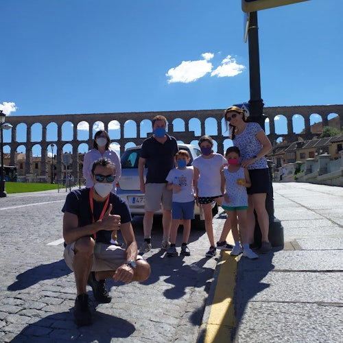 A group of people, all wearing masks, pose for a photo in front of an ancient aqueduct on a sunny day.