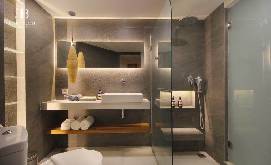 Modern one bathroom in the Mezzanine apartment suite at Echo Beach, Canggu, Bali, with a glass shower, floating vanity, and stone tiles.