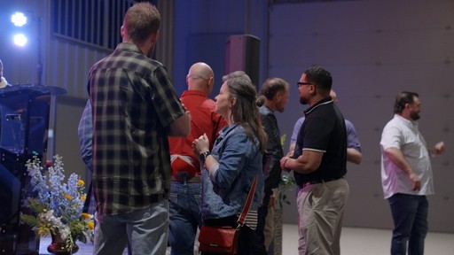 A group of four people standing outside a building, engaging in conversation, with cars parked nearby.