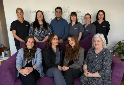 The Team of Dentist and Nurses at Chester Cosmetics & Dental Care sat on a couch and some standing behind